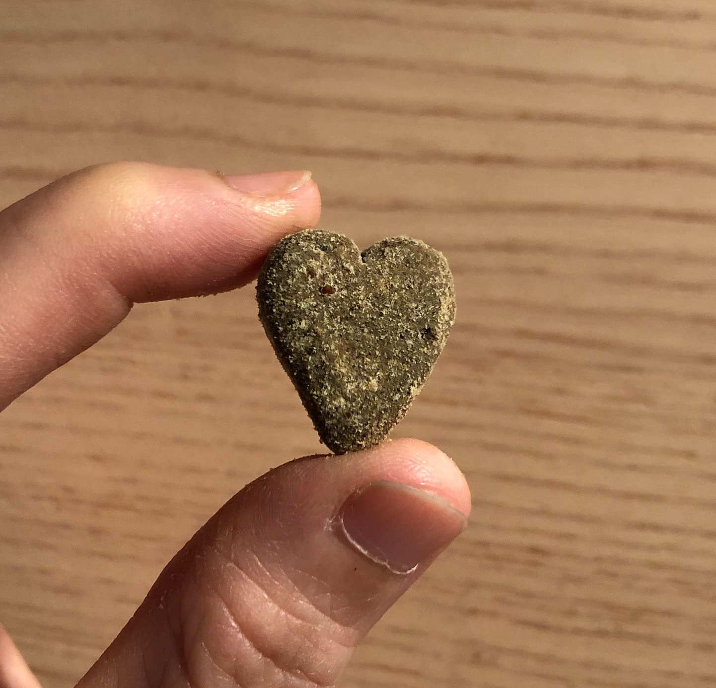 Heart-shaped object held between fingers against a wooden background